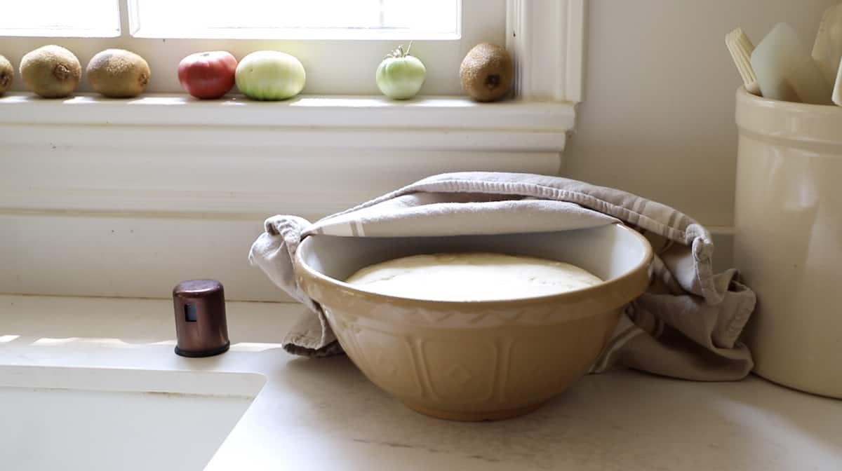 Pizza dough rising in a bowl under a window