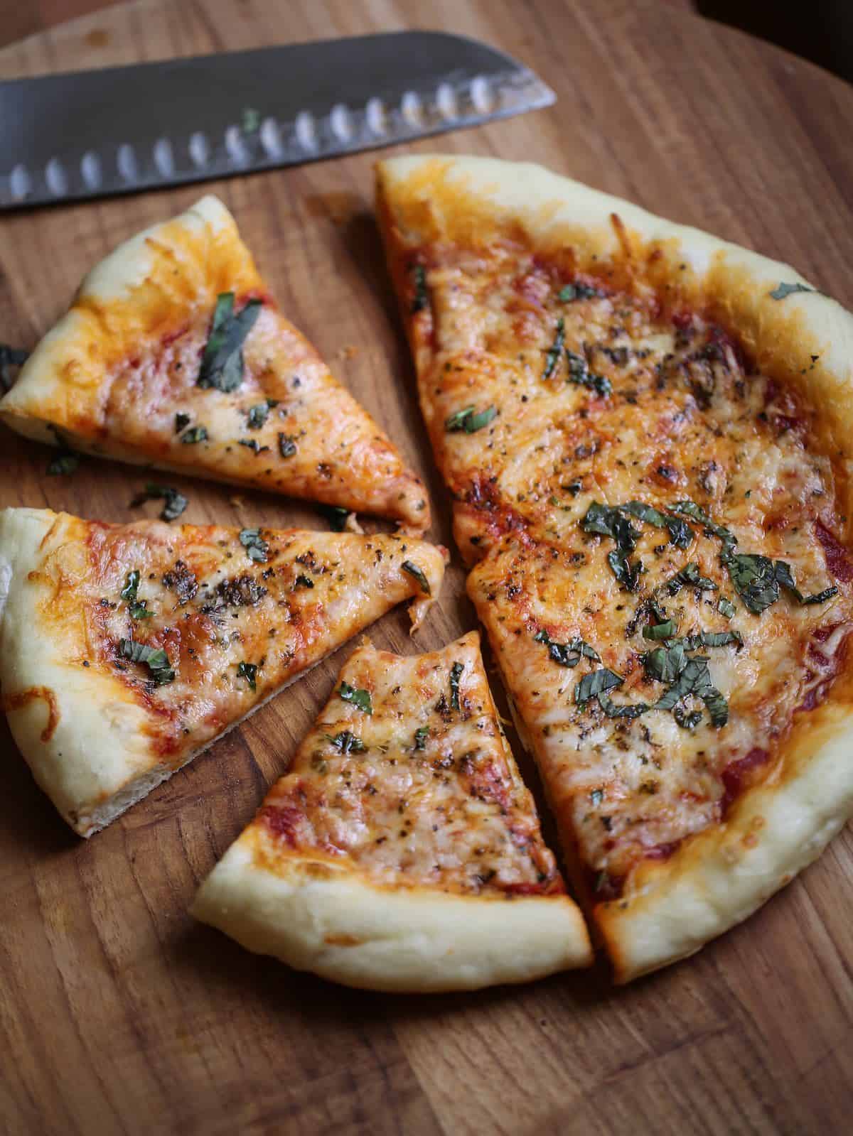 vertical image of sliced cheese pizza on a board