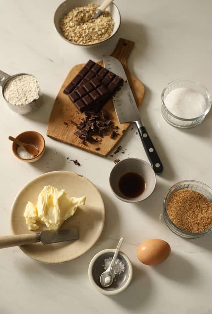 Butter, eggs, brown and white sugar, vanilla, dry ingredients and dark chocolate on a counter.