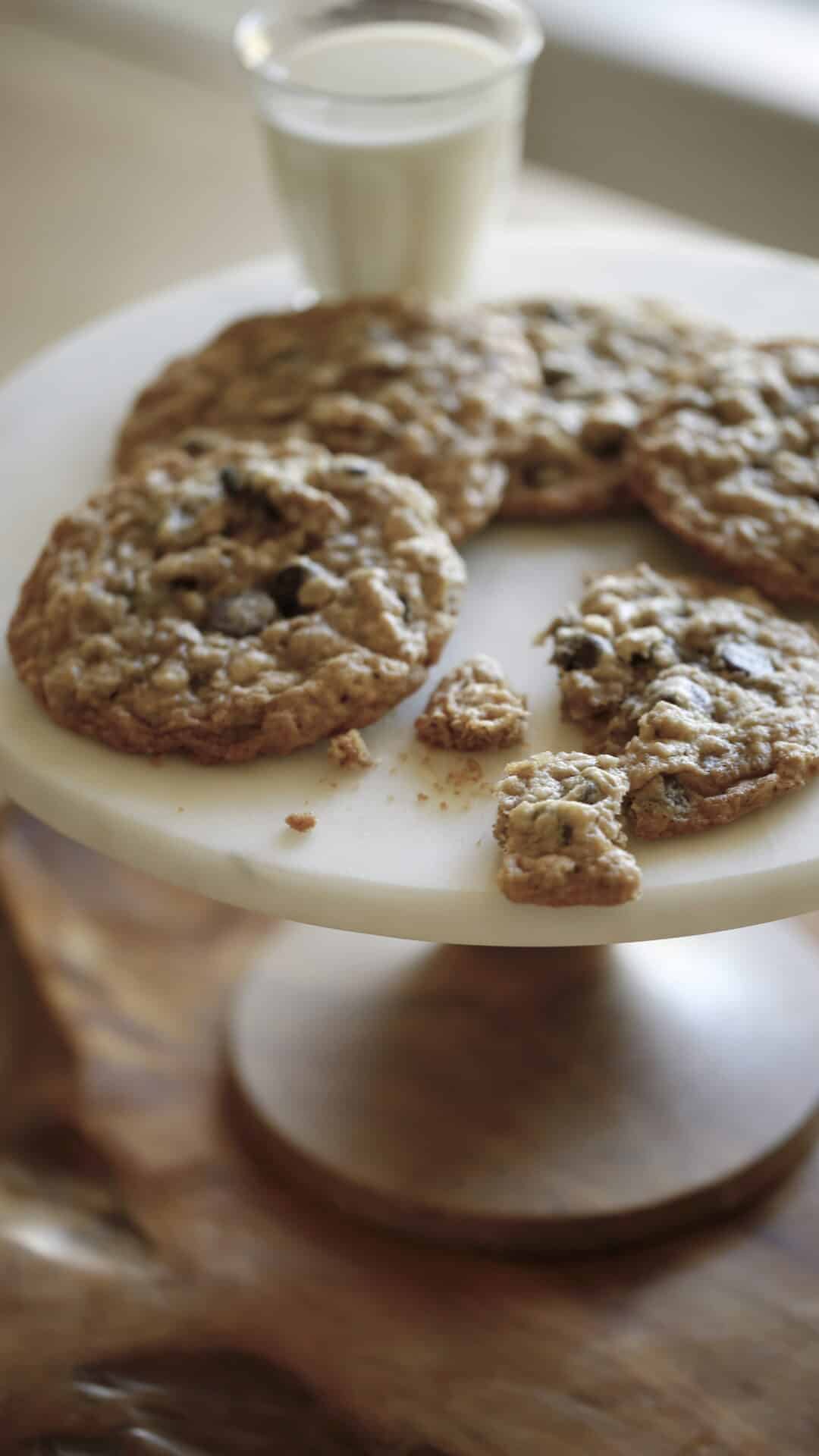 a vertical image of a marble cake stand with cookies and milk on top