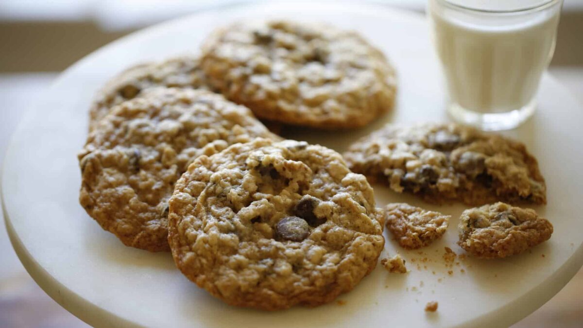 a marble cake stand with Oatmeal cookies broken and whole and a small glass of milk