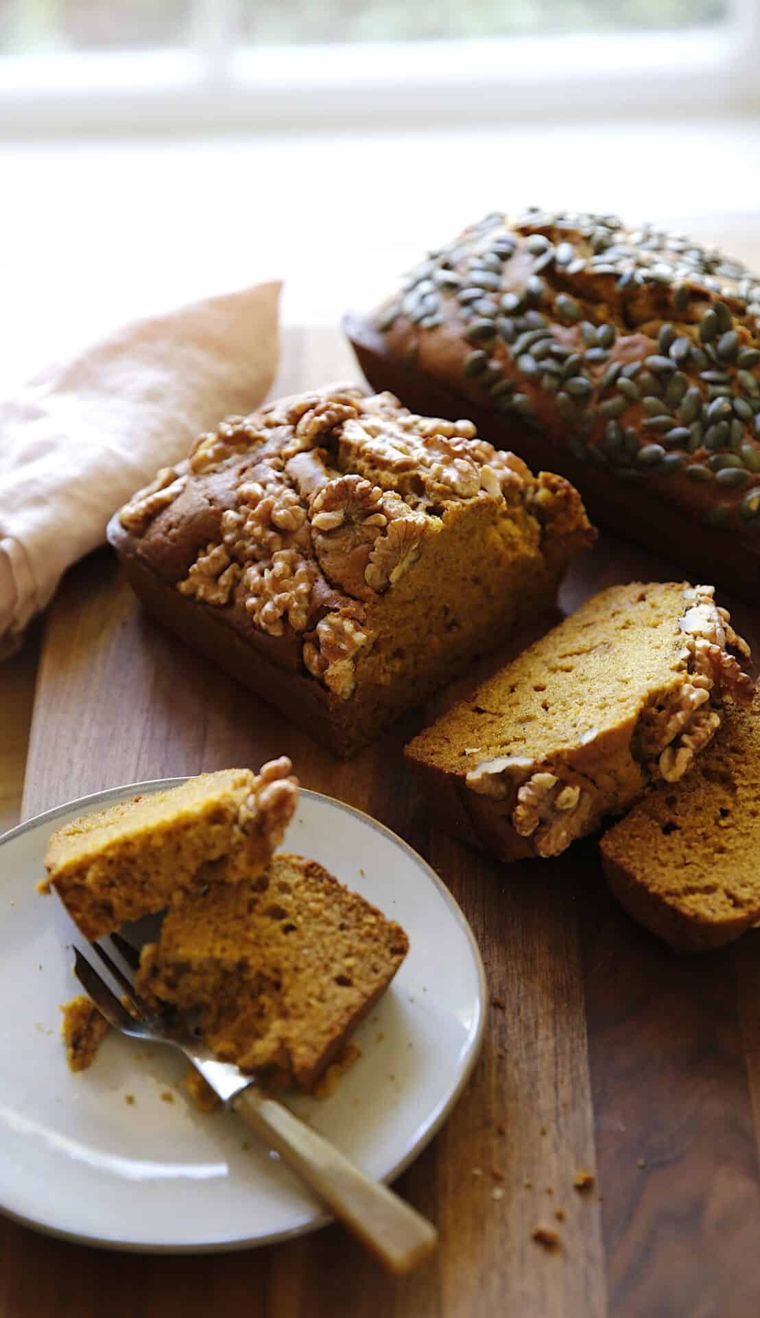 2 loaves of pumpkin bread sliced and a slice placed on a plate with a fork