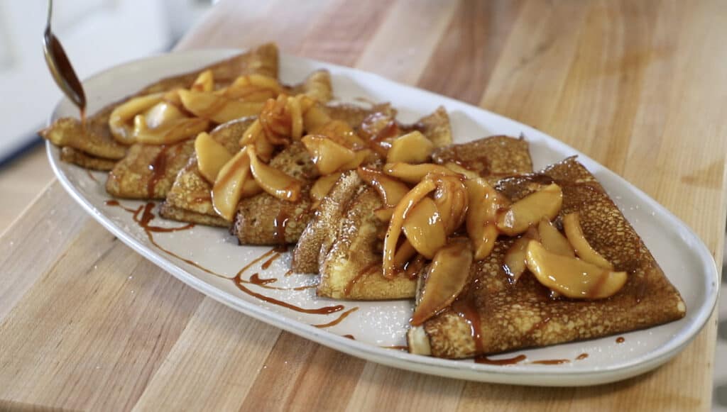a platter of crepes with apples and caramel sauce