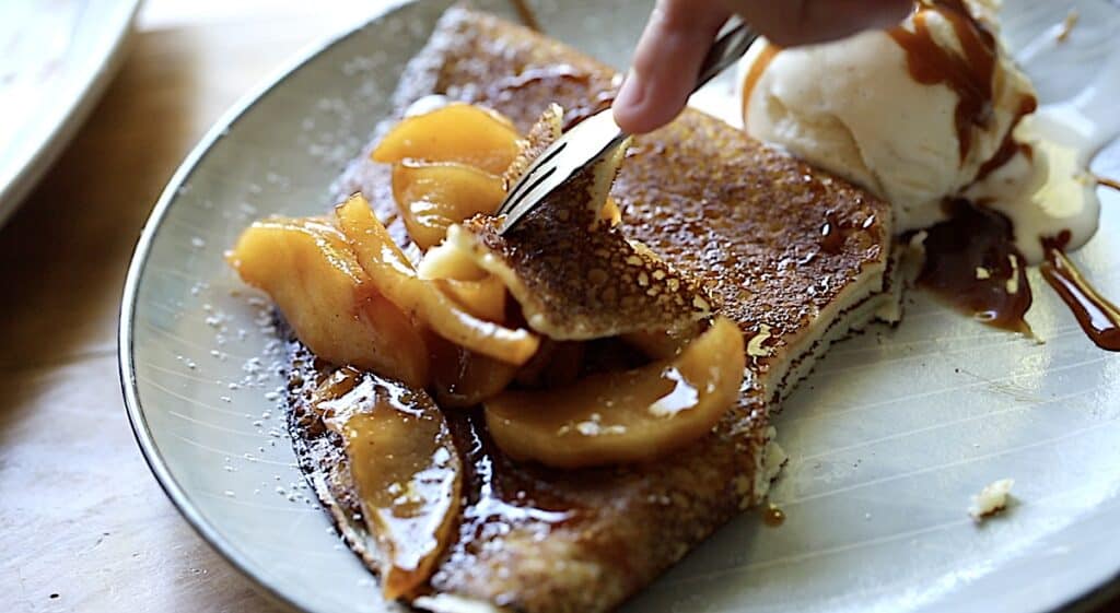 Fork taking a bite from an apple crepe with ice cream 