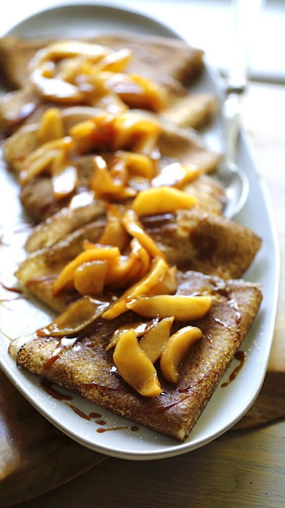 Vertical Image of crepes on a long platter stacked and served with apples on top