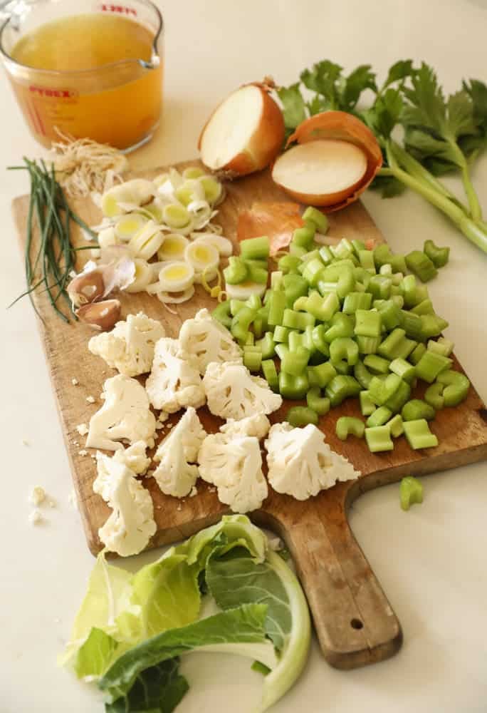 chopped celery, onion, leeks and garlic on a cutting board,