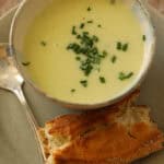 celery soup with chives on a plate with a crusty baguette.
