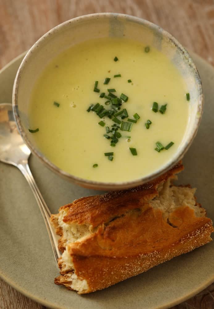 celery soup with chives on a plate with a crusty baguette.