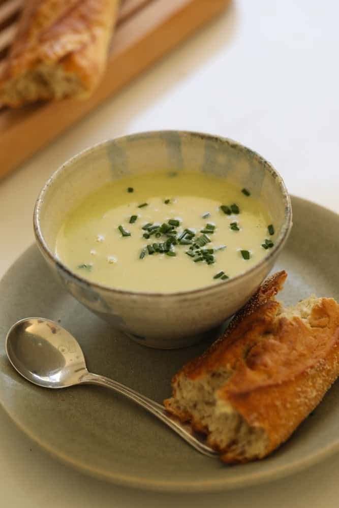 a bowl of soup with a plate and baguette.