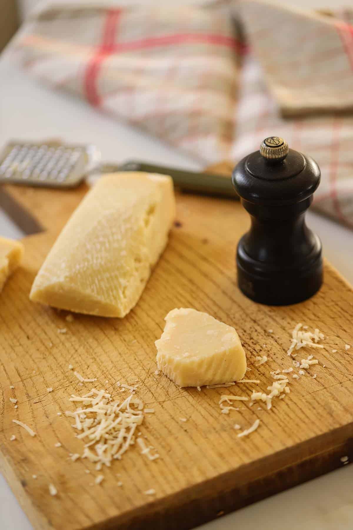 Wedges of parmesan cheese on a cutting board with a pepper grinder.