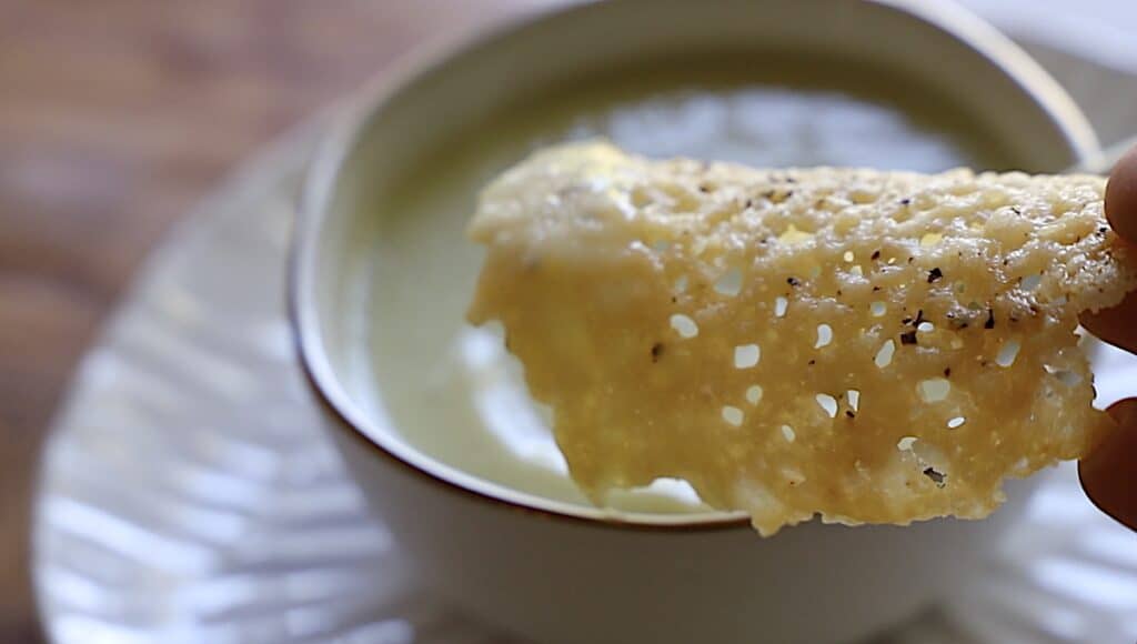 a parmesan tuille dipped into a cream of celery soup