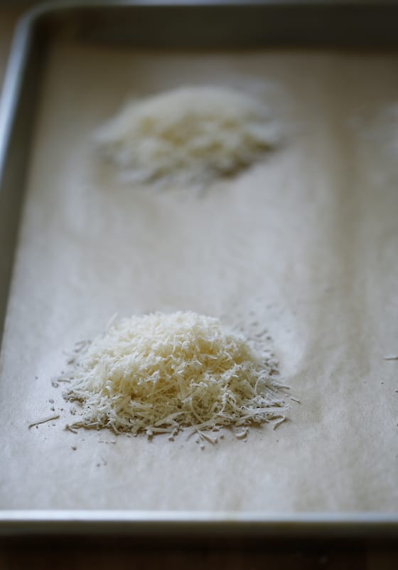 a vertical shot of grated parmesan cheese mounds on a baking sheet lined with parchment paper