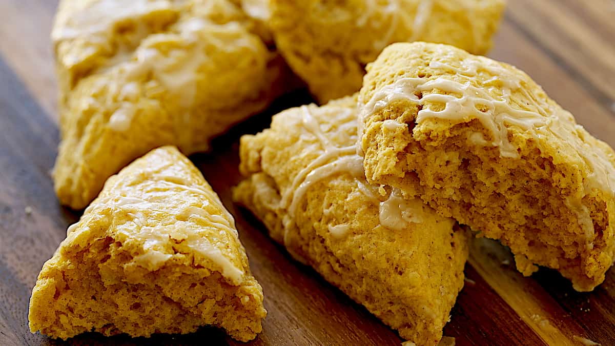 a few pumpkin scones on a board with one cut in half to see interior fluffy texture