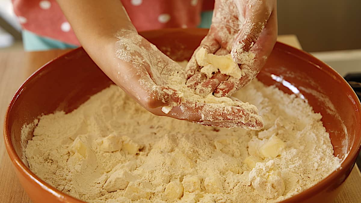 hands in a bowl combinning butter and flour mixture in to crumbles