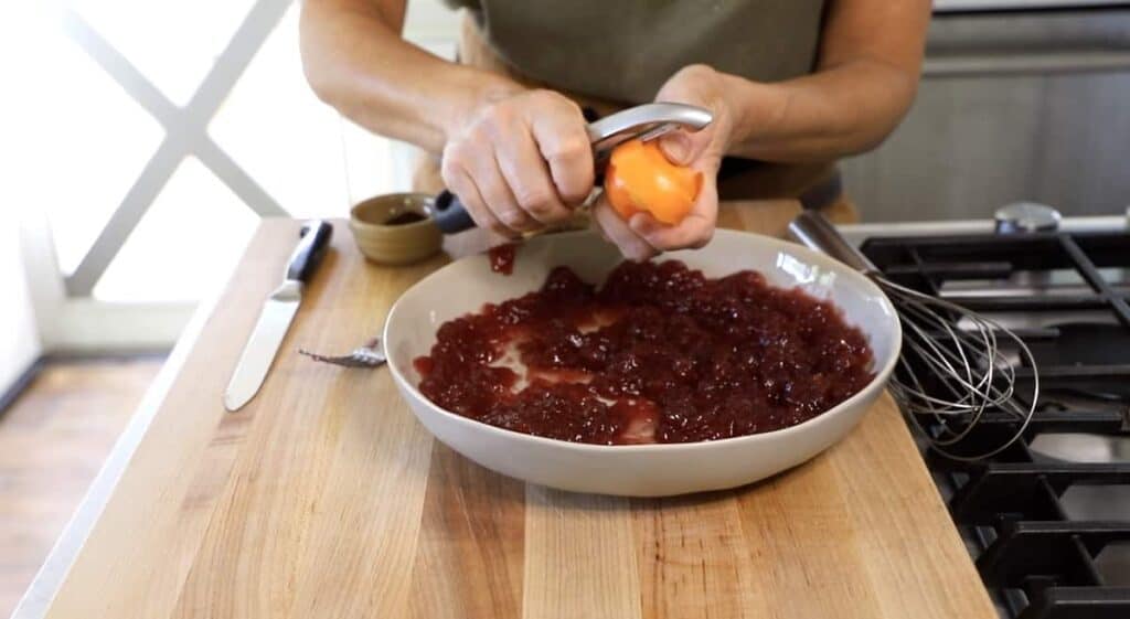 a person peeling an orange into cranberry sauce