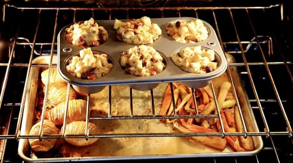 interior of an oven with stuffing muffins on top rack and a sheet pan of carrots and potatoes on the lower rack