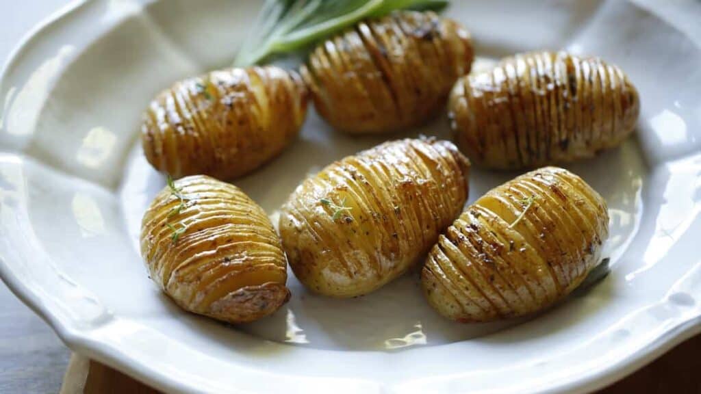 Perfectly Roasted Hasselback Potatoes on a white platter with a garnish of fresh sage