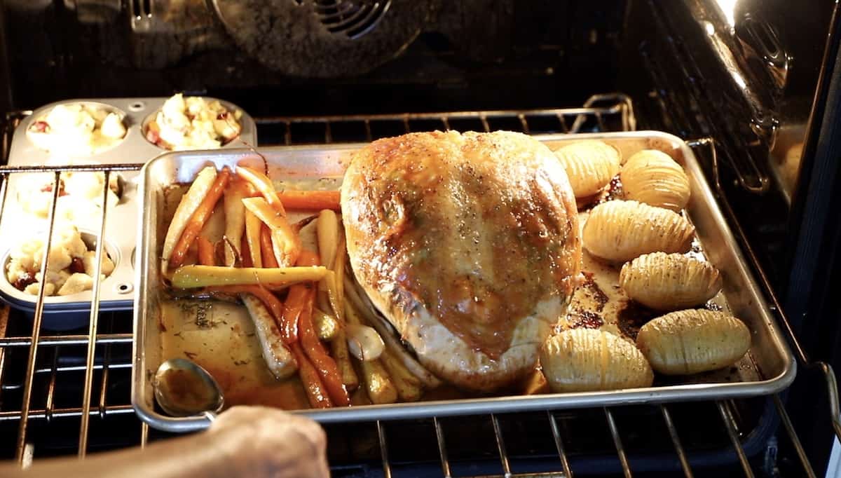 a person spooning the pan gravy from a sheet pan of a Turkey and vegetables roasting in the oven