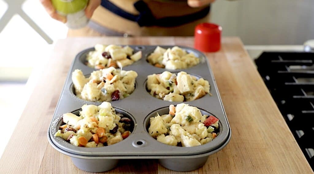 a Jumbo Muffin tin with stuffing muffins filled and a can of olive oil spray spraying the tops of them