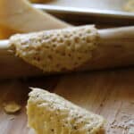 a vertical image of a parmesan tuile on a cuttng board with a tuille around a rolling pin on background
