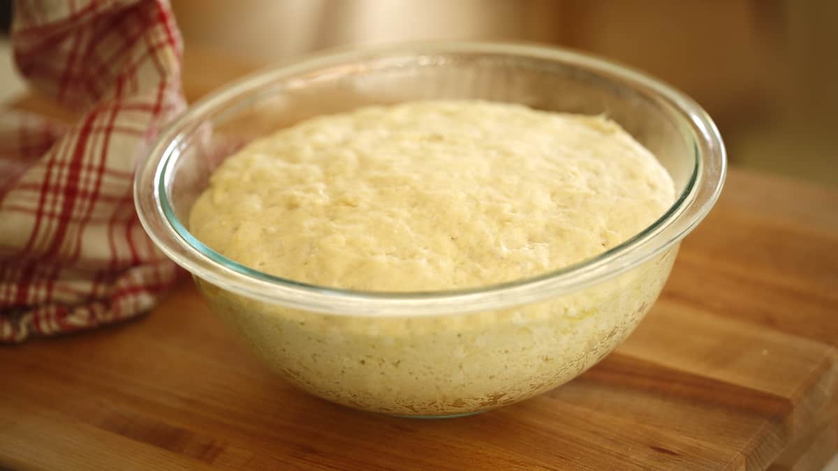 a clear bowl with risen dough in on on a cutting board 