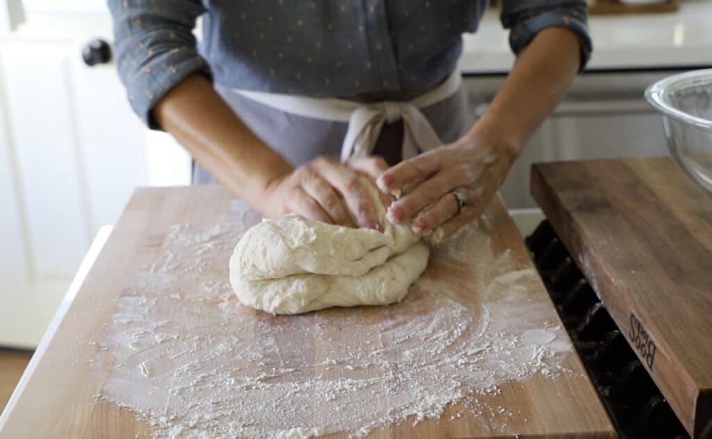 kneading bread dough on a cutting board with flour