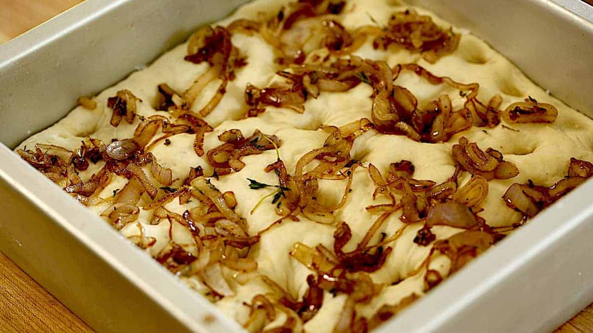 focaccia dough in a cheesecake pan topped with caramelized shallots