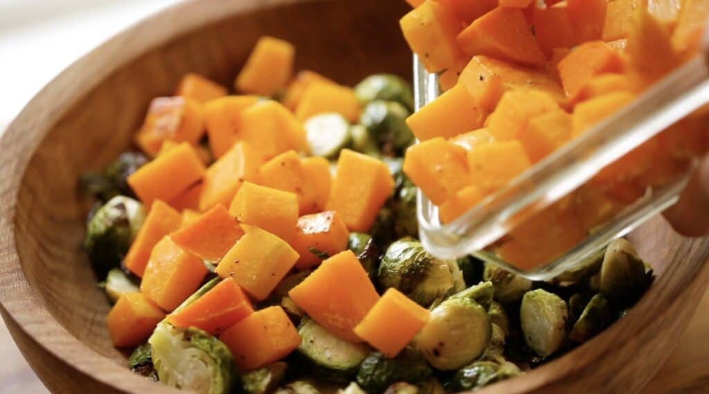 adding cooked butternut squash cubes to a salad bowl with Brussels sprouts