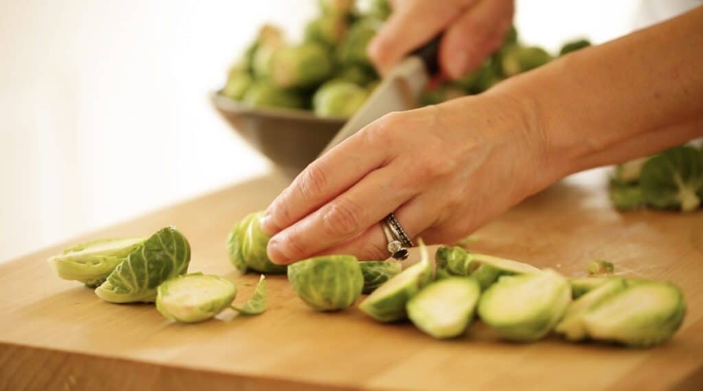 slicing brussle sprouts in half on a cutting board