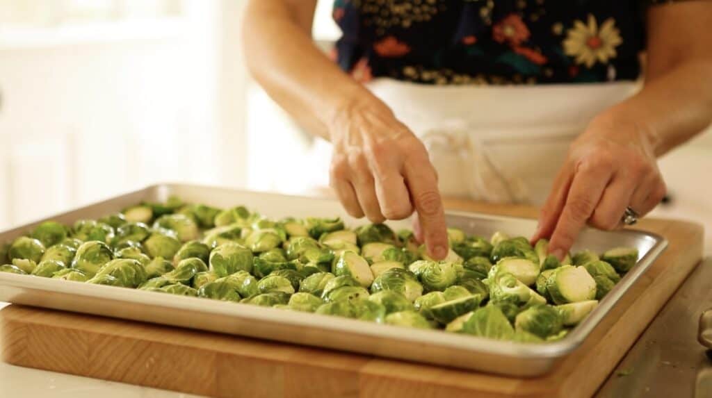 a person adjusting cut brussle sprouts on a sheet pan 