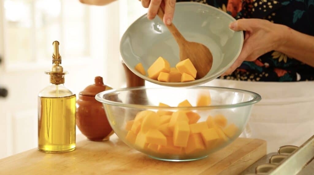 Adding cubed butternut squash to a clear bowl 