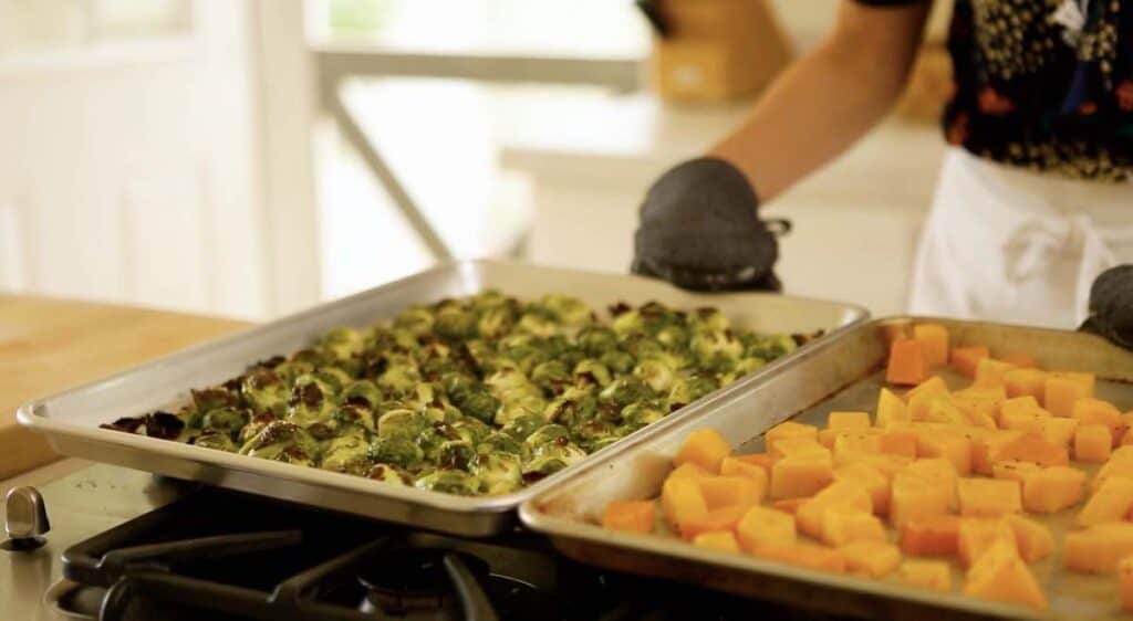 a person placing sheet pans filled with vegetables on a cooktop