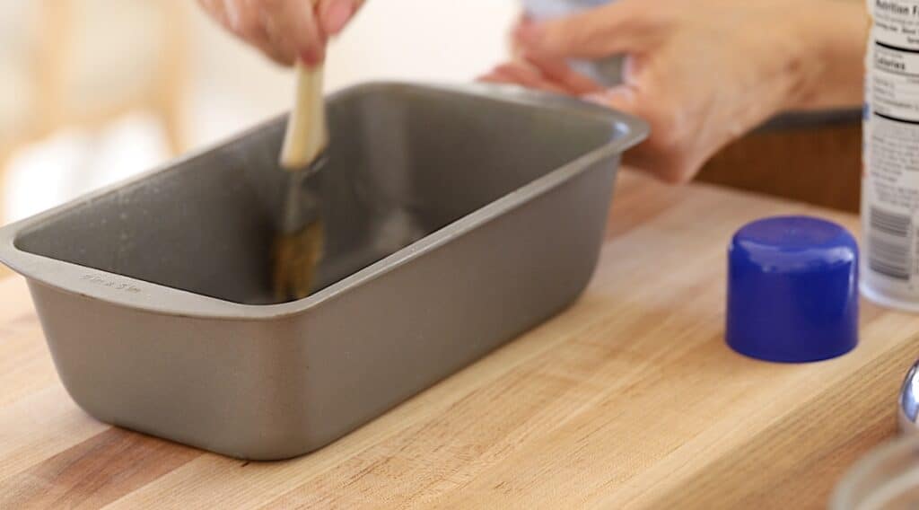 A person distributing baking spray with a pastry brush