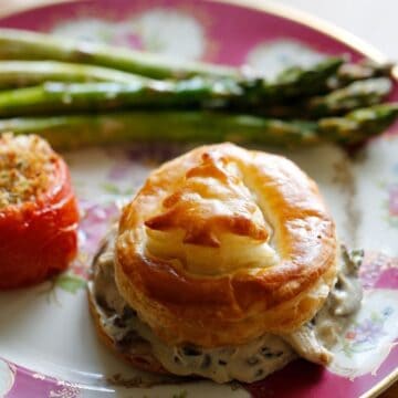 Bouchee a la reine in puff pastry on a plate with a roasted tomato and asparagus