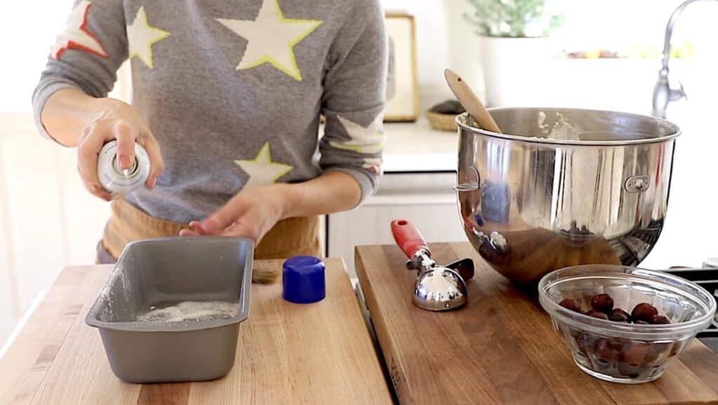 a person spraying a loaf pan with baking spray