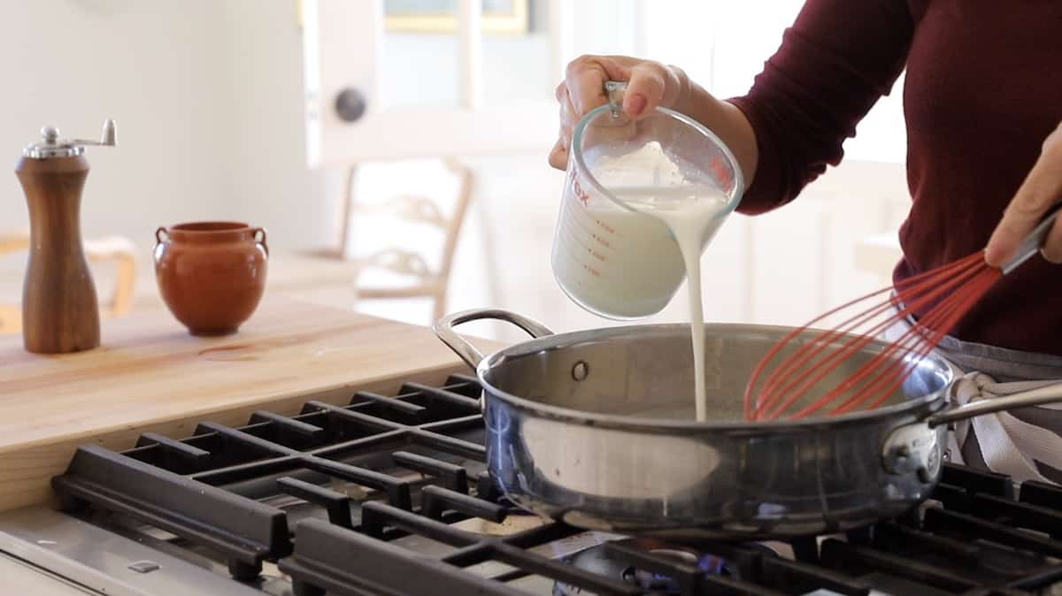 a person adding milk to a large skillet