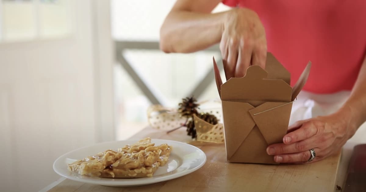 a person packaging up peanut brittle in a Chinese takeout box