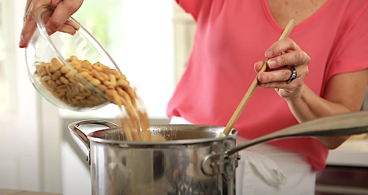 a person adding peanuts to a pot of syrup