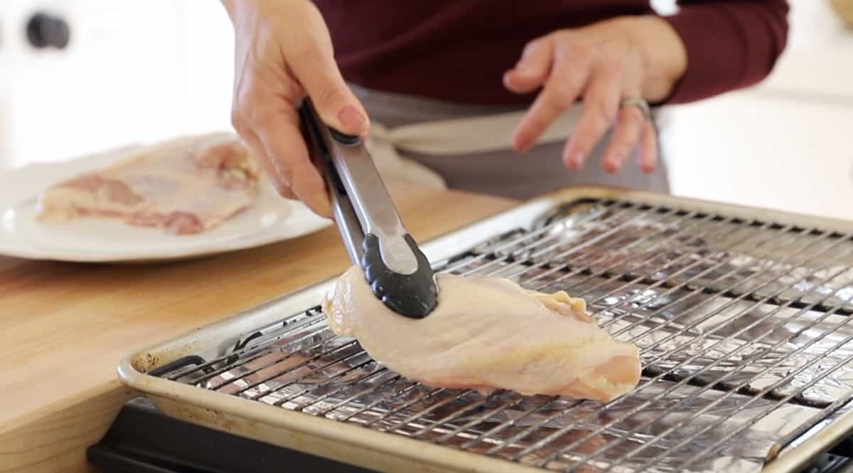 adding chicken breast to a sheet pan with rack with a pair of tongs