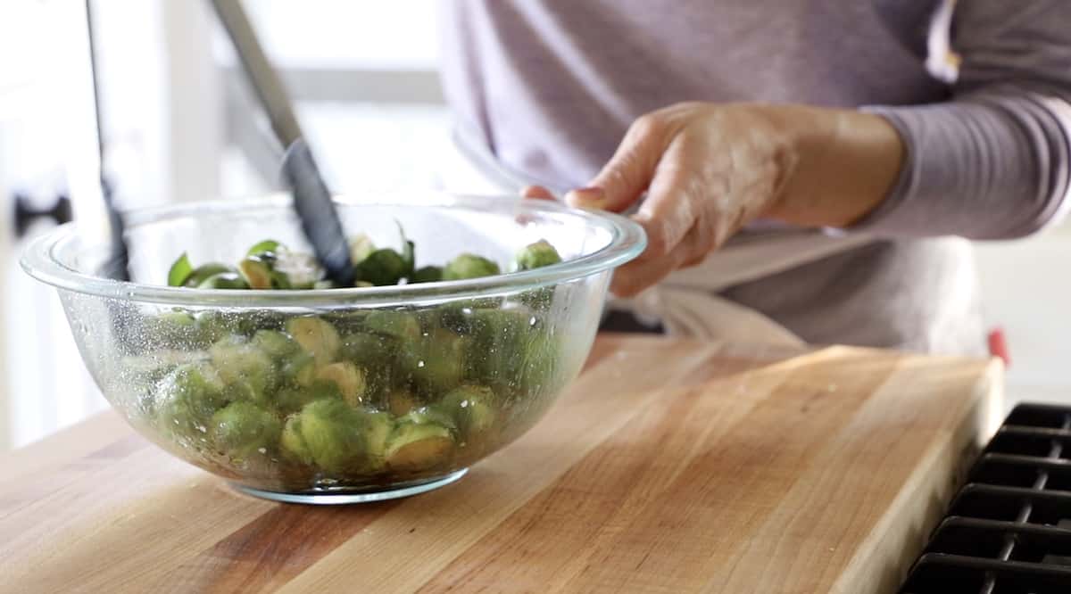 a person tossing brussel sprouts in a bowl with tongs