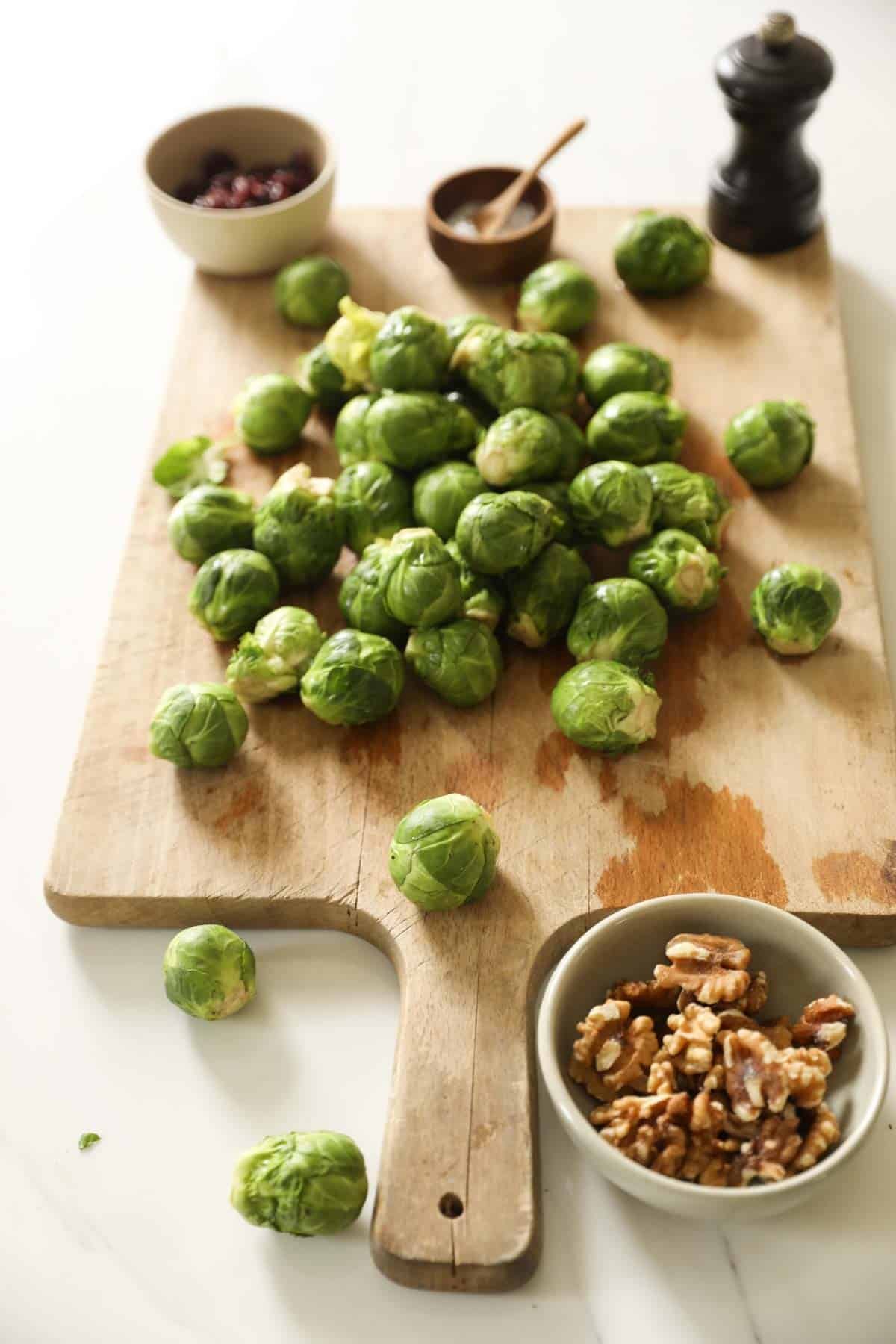 Brussels sprouts, salt, pepper, walnuts and cranberries on a cutting board.