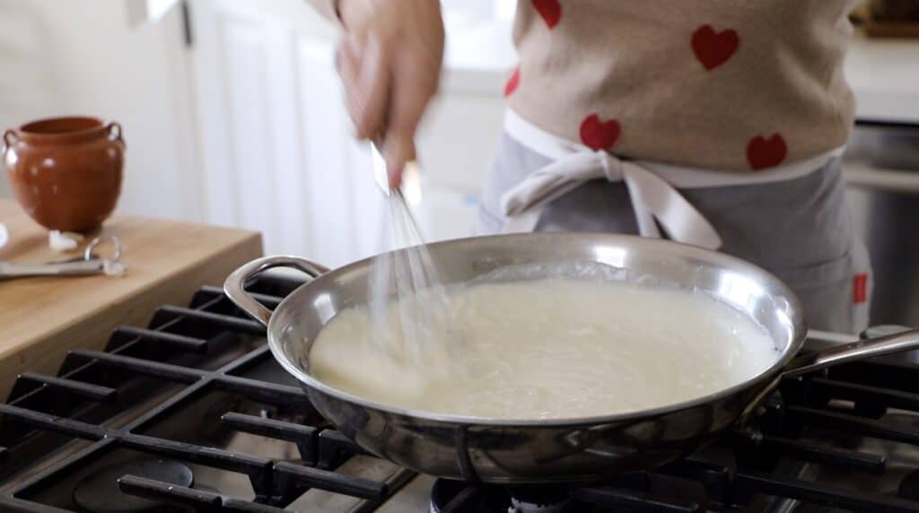 a person making bechamel sauce in a skillet