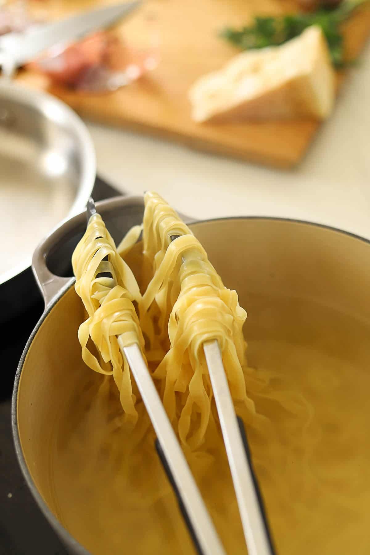 Cooked Pasta hanging over tongs in a pot.