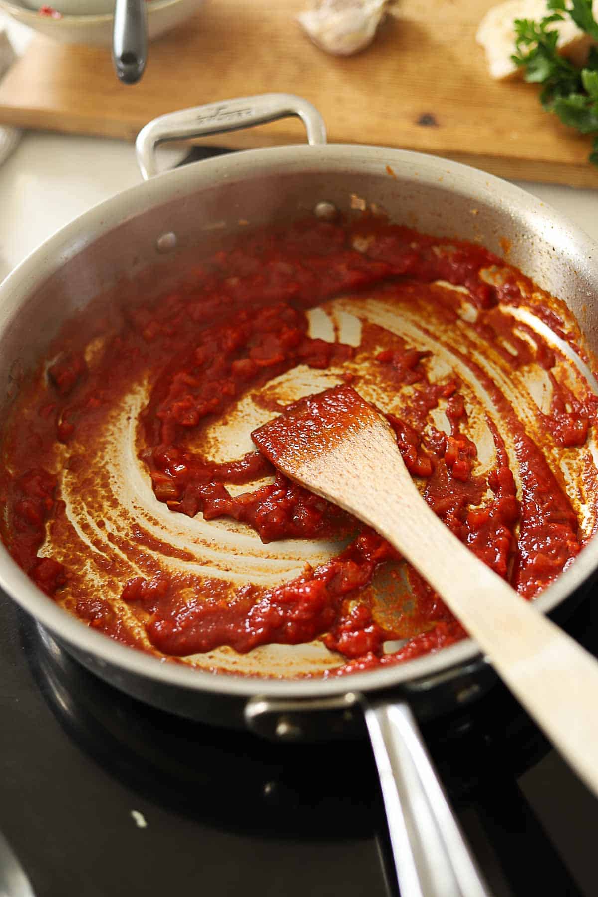 Shallots and Tomato Paste in a skillet with a wooden spoon.