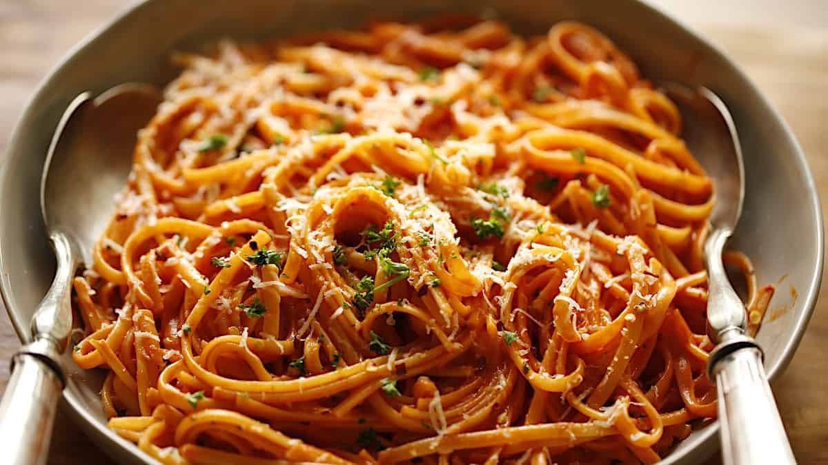 a close up of grated parmesan cheese and chopped parsley on linguine with a creamy tomato sauce