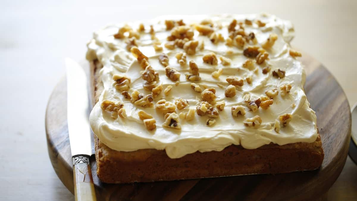 a whole banana cake with cream cheese frosting topped with walnuts on a board