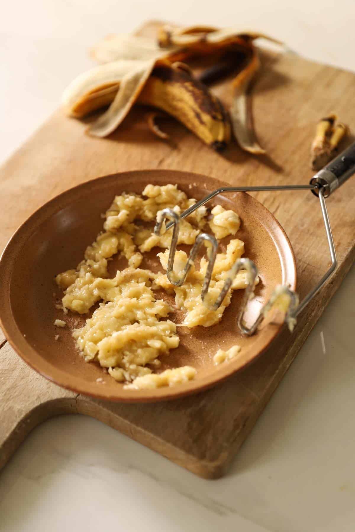 ripe bananas mashed with a potato masher in a bowl.