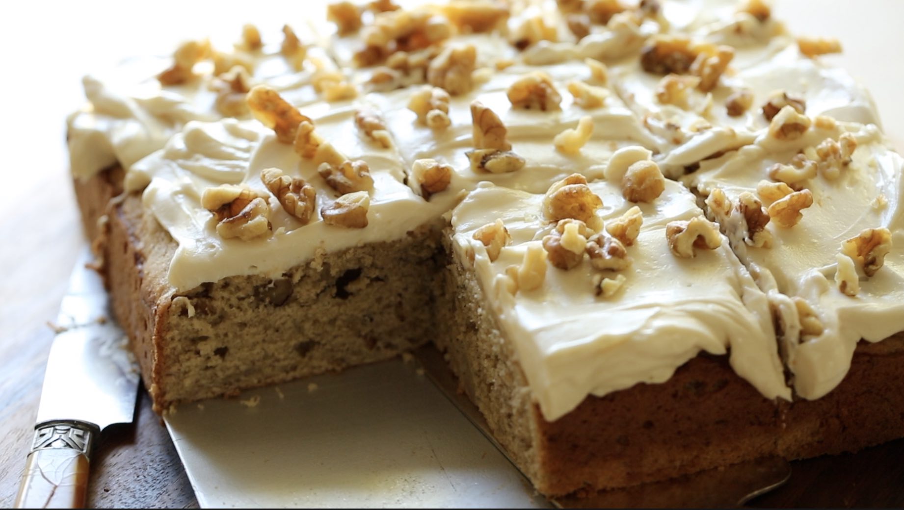 A whole banana cake with cream cheese frosting topped with nuts