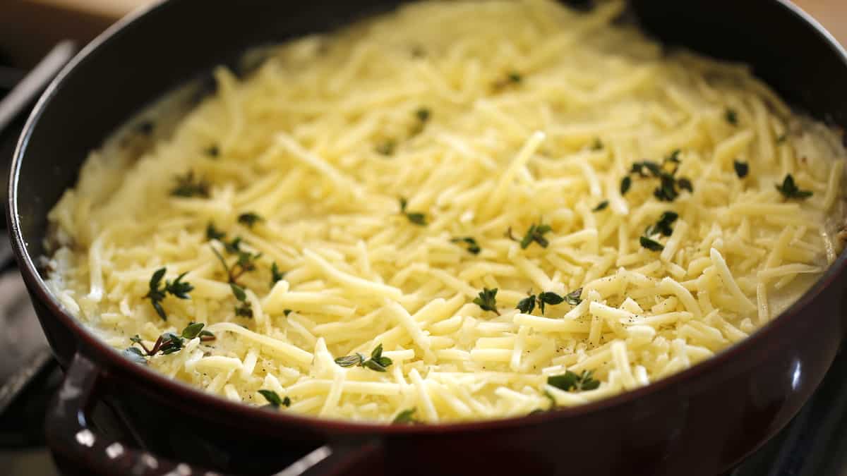 Casserole dish topped with potatoes and covered in Gruyere Cheese and fresh Thyme