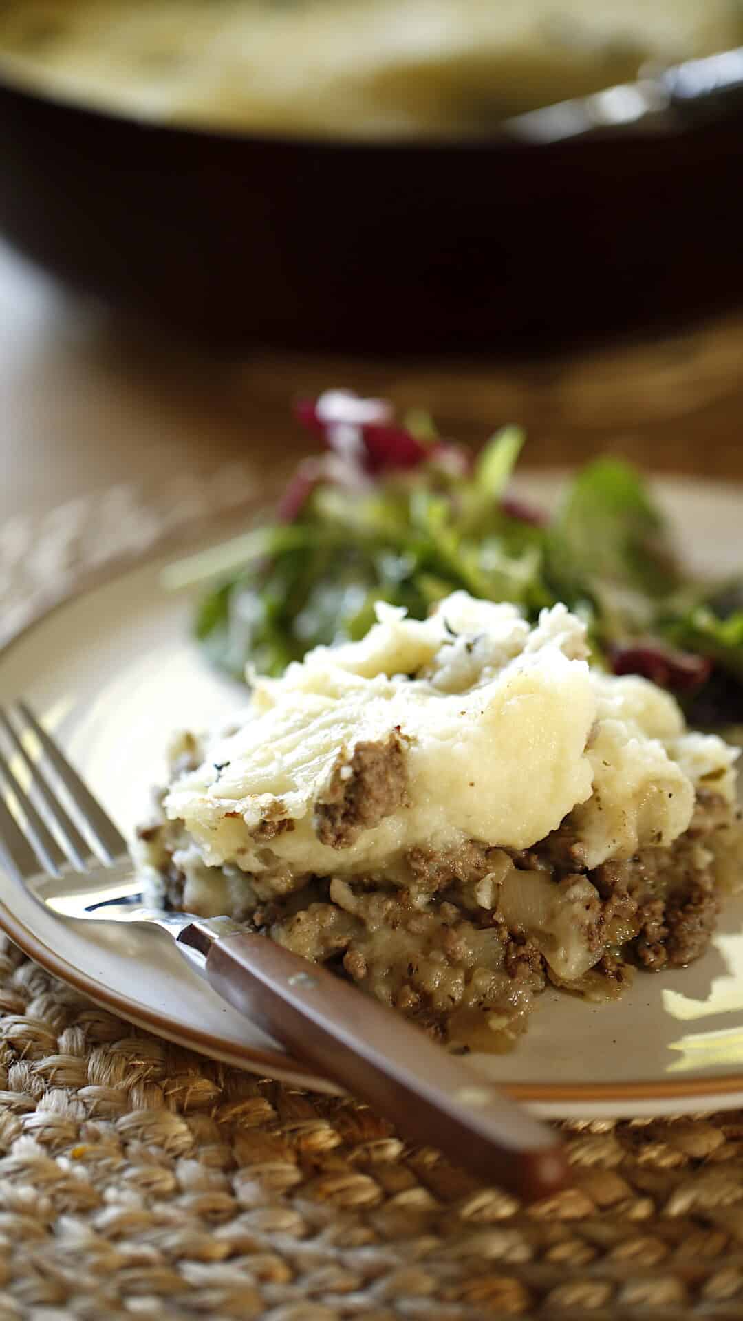 a potion of hachis parmentier on a plate with a side salad and casserole dish in the background